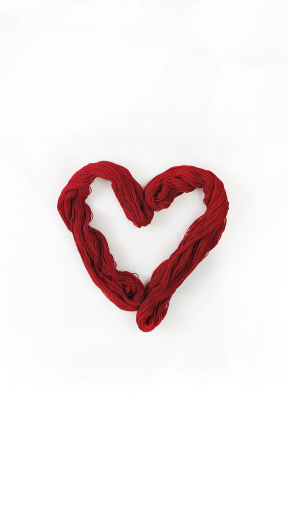 A white background two skeins of red yarn twisted into a heart shape