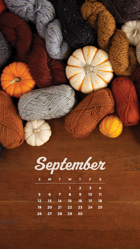 A large pile of various yarn in fall colors (rust, pumpkin, gray, maroon), along with assorted decorative pumpkins. A Sept 2021 calendar at the bottom, over a wooden background.
