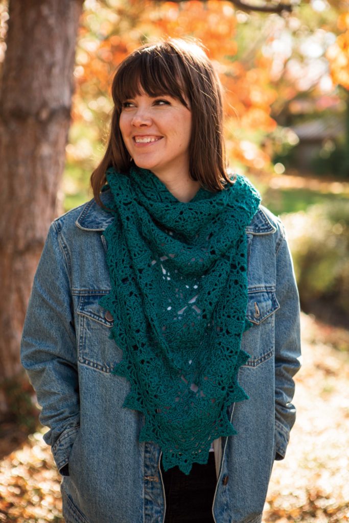 An image of a model wearing a teal colored crocheted shawl around her neck