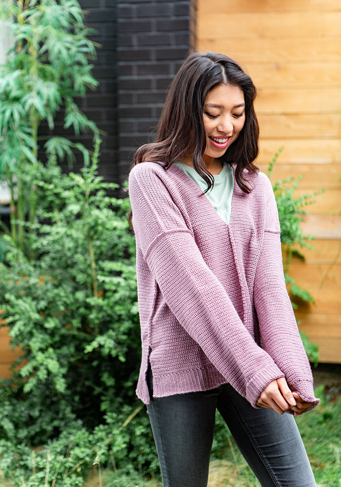 A Model wearing a crochet sweater and looking down at her sleeves.