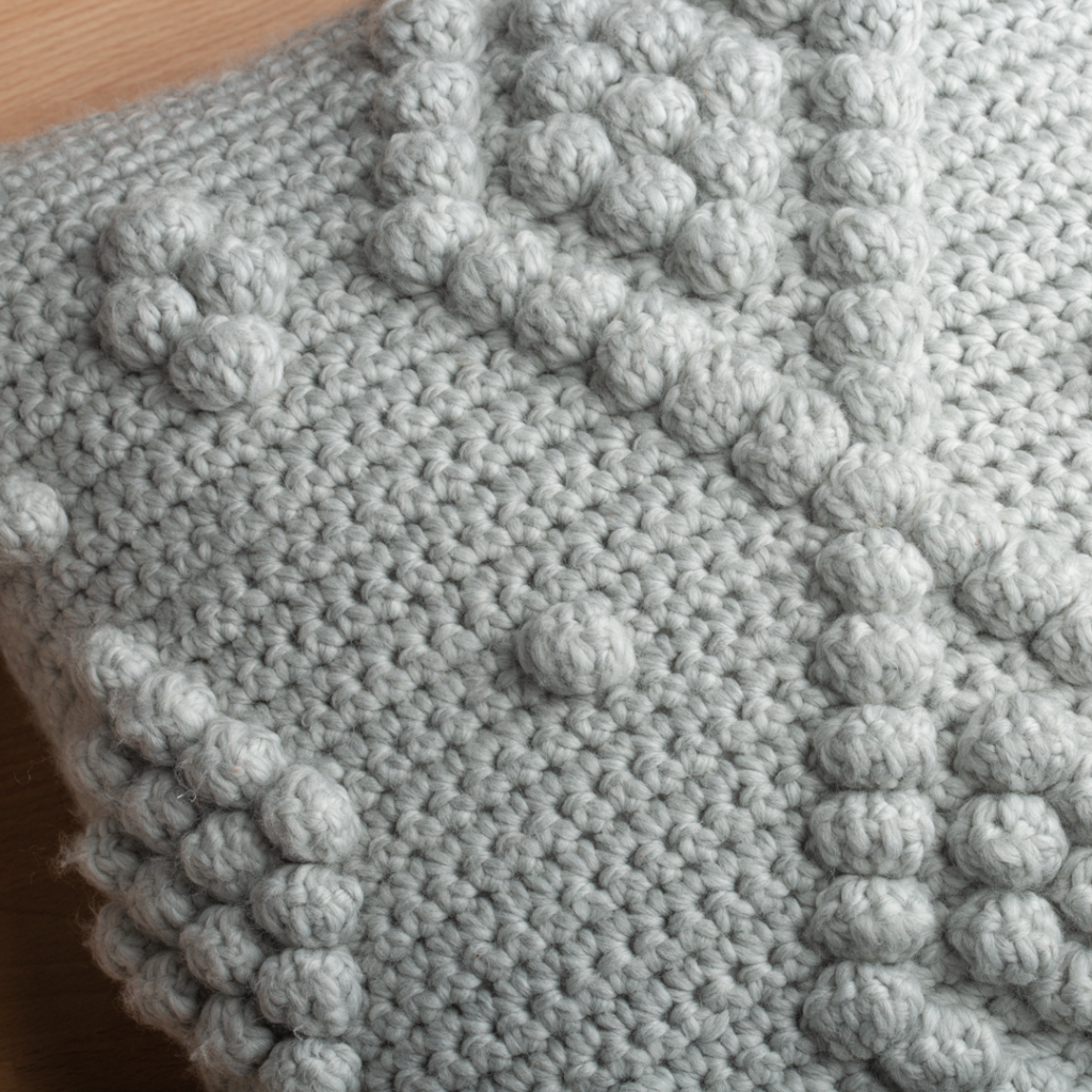 Closeup of crochet texture in gray featuring bobble stitches in a diamond formation. One of our free home decor crochet patterns.
