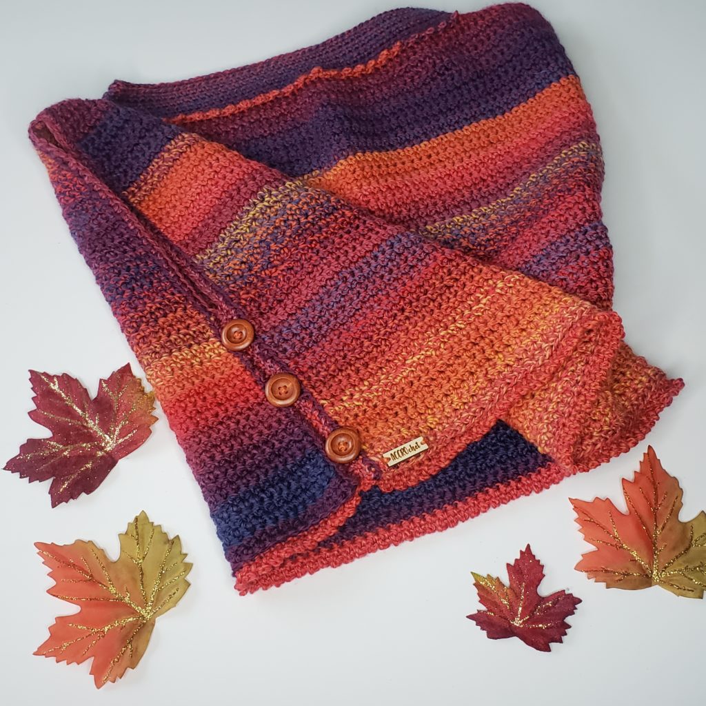 Boxed In crochet shrug pattern by ACCROchet. A top-down view of the Boxed In shrug - it has a sunset colored gradient thanks to Chroma Twist yarn, and is surrounded by sparkly fall leaves.