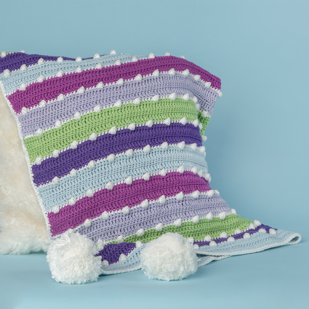 Holiday lights blanket shown draped over a fur pillow, a free crochet pattern from crochet.com