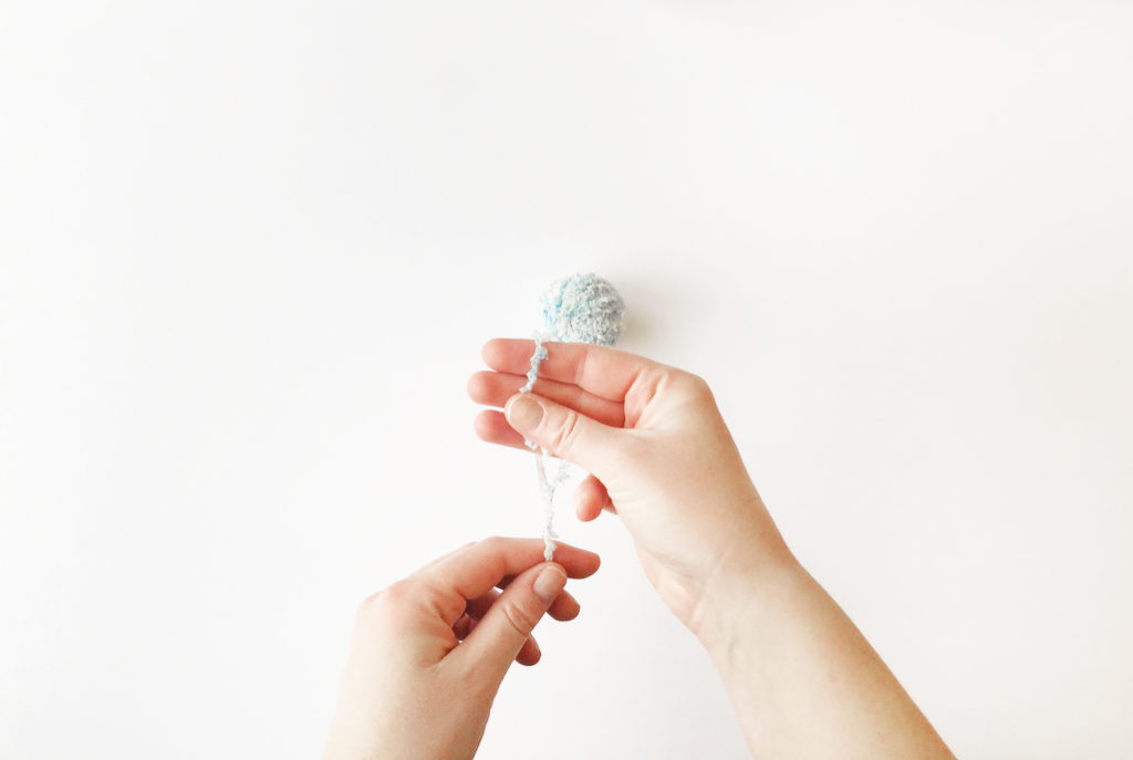 A top-down shot of hands wrapping fur yarn around 3 fingers to make a pom-pom