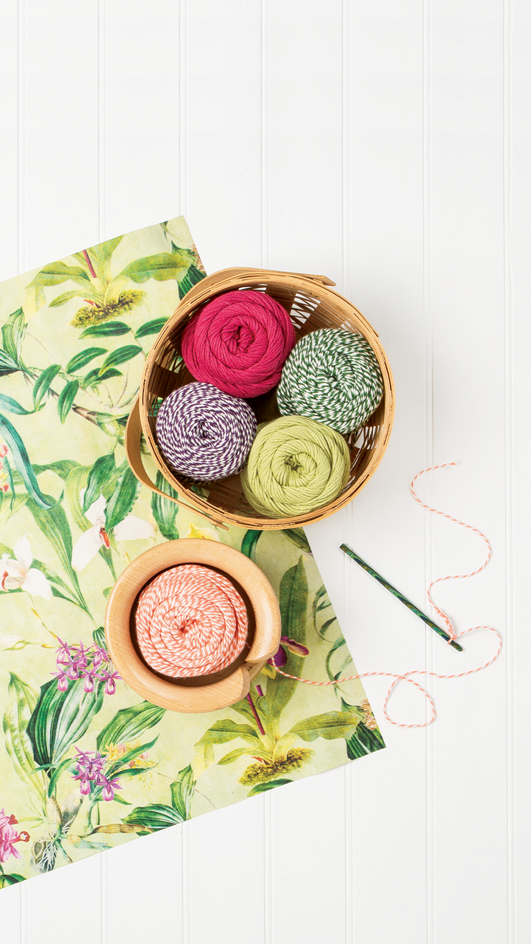 A top-down view of a white background with a floral pattern paper on it, with a yarn bowl filled with colorful cotton yarn.
